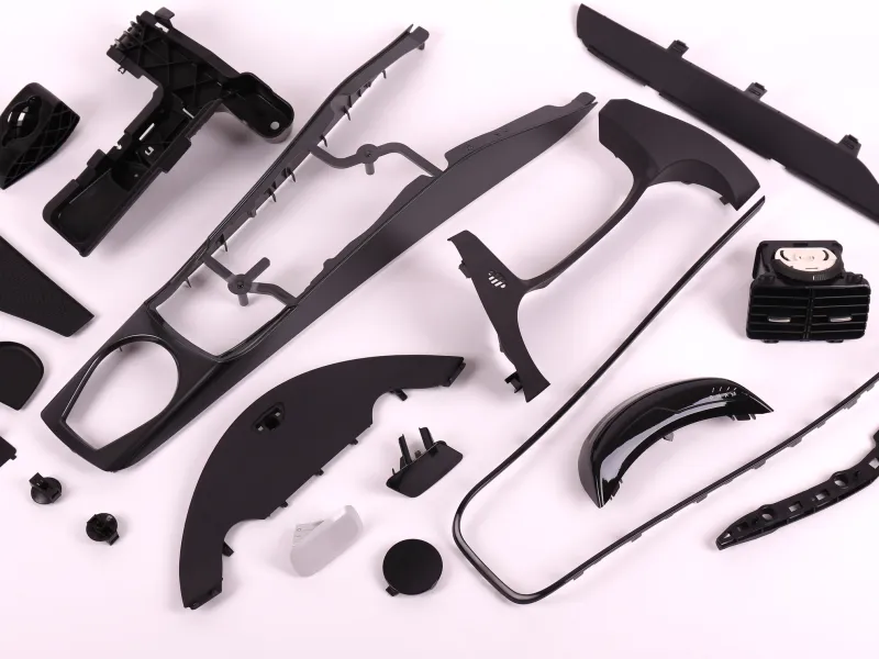 A range of black plastic interior parts by RH Kunststofftechnik GmbH, including a centre console, air vent, door handle trim and seals for the vehicle interior.