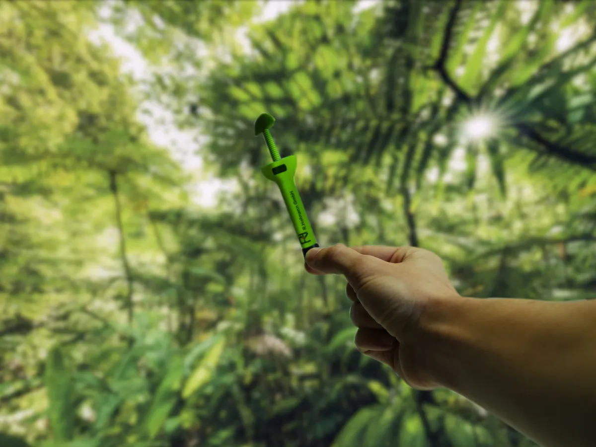 A component made from recyclable Green PE by RH Kunststofftechnik GmbH, held up to the sunlight in a forest.