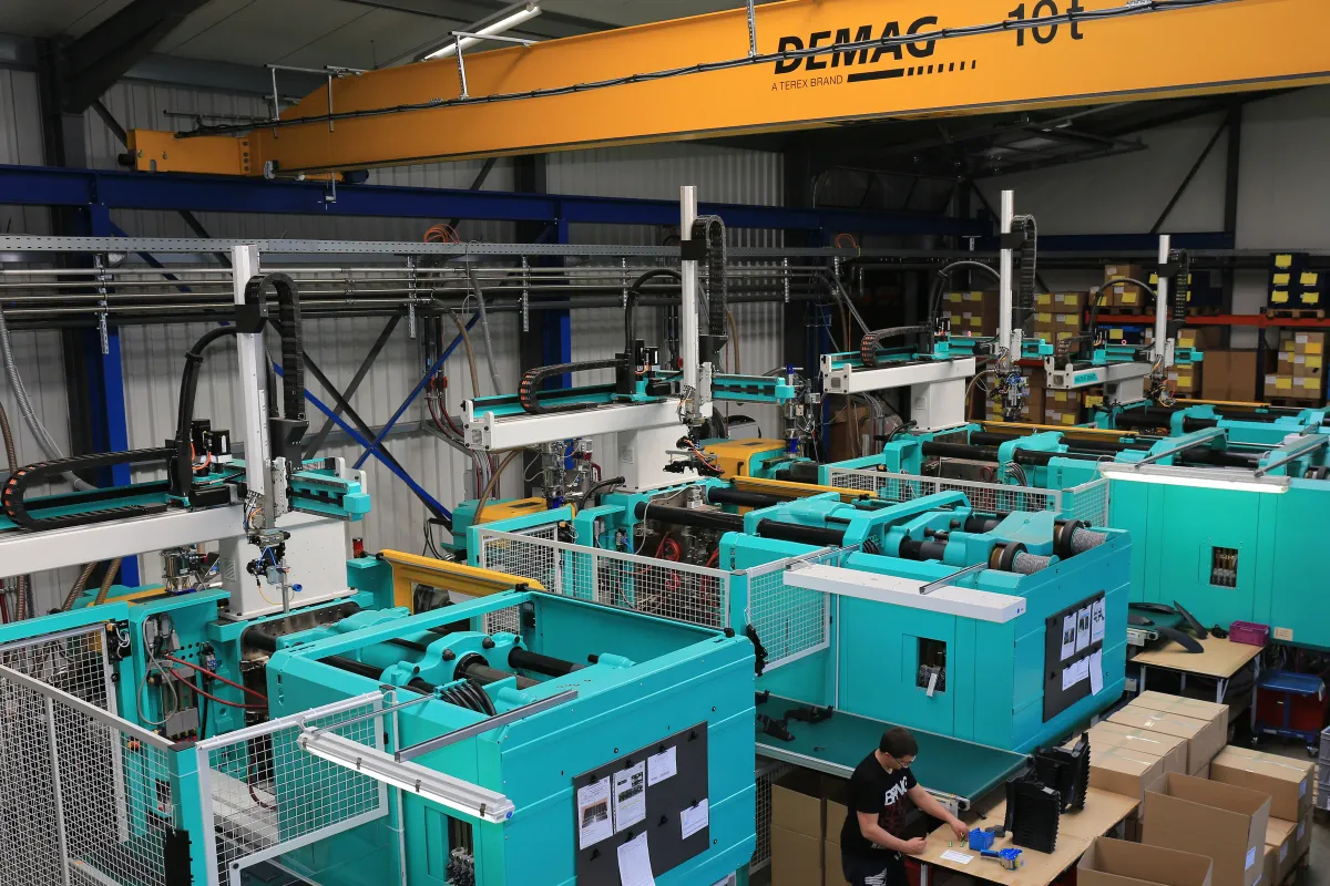 View into the RH Kunststofftechnik GmbH production hall with several injection moulding machines, handling robots and an overhead crane.