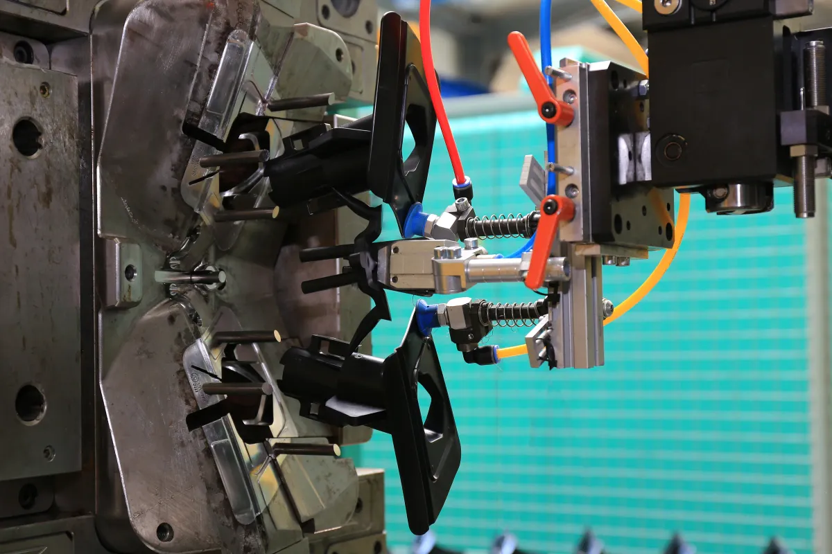A handling robot removing freshly moulded plastic components from an open injection mould.