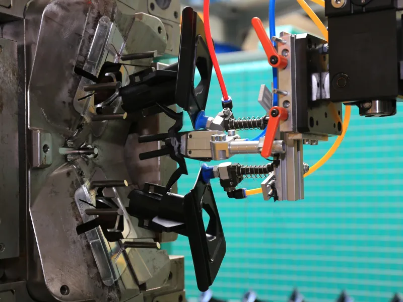 A handling robot removing freshly moulded plastic components from an open injection mould.